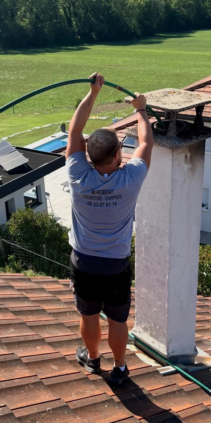 M. Robert sur une toiture en tuiles, canne de ramonage engagée dans le conduit de cheminée